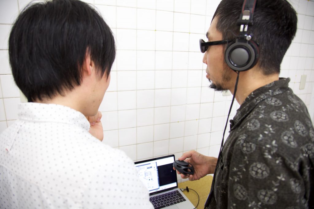 ヘッドフォンをつけた参加者にメンバーの岡田が説明を行う。